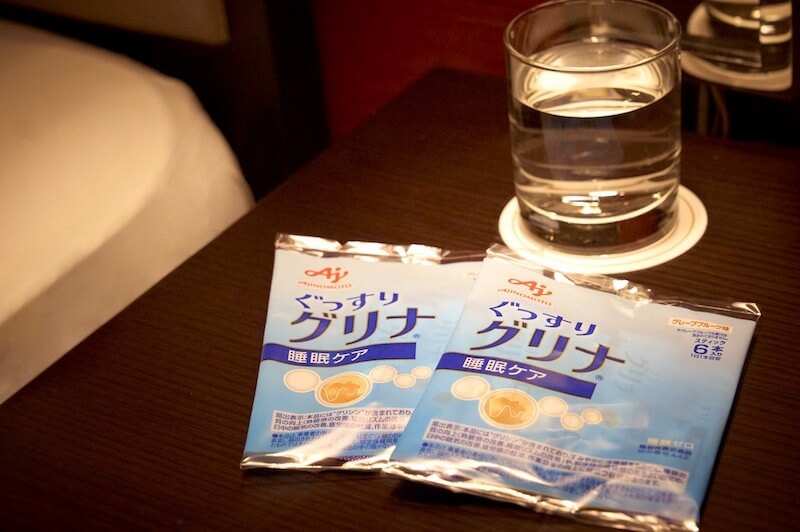 ぐっすりと質の良い睡眠をサポートするサプリ「グリナ」が、水の入ったグラスと一緒に置かれている写真