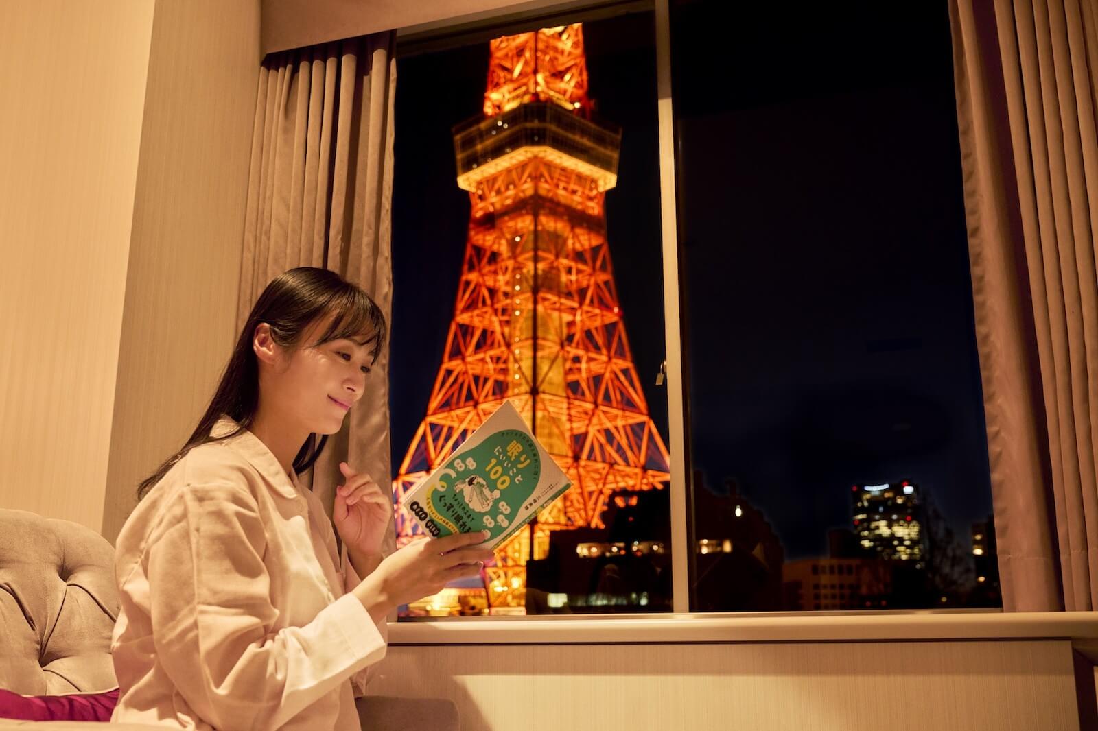 客室で本を読む人と、客室の窓から夜の東京タワーが見える写真