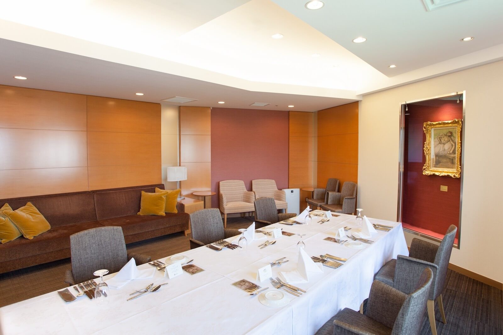 ホテル内の個室ダイニングまたは宴会場の室内。白いクロスをかけた長テーブルに食器がセッティングされ、椅子とソファ席が配置されている。奥の壁には額装された絵画が飾られ、落ち着いた雰囲気の空間。