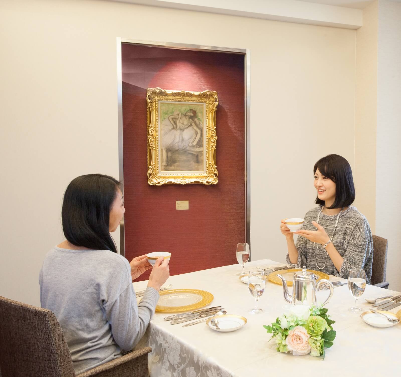 特別ラウンジで向かい合って食事を楽しむ2人の女性。壁面にはドガの《踊り子》が展示され、名画を鑑賞しながら食事ができる特別プランの様子。
