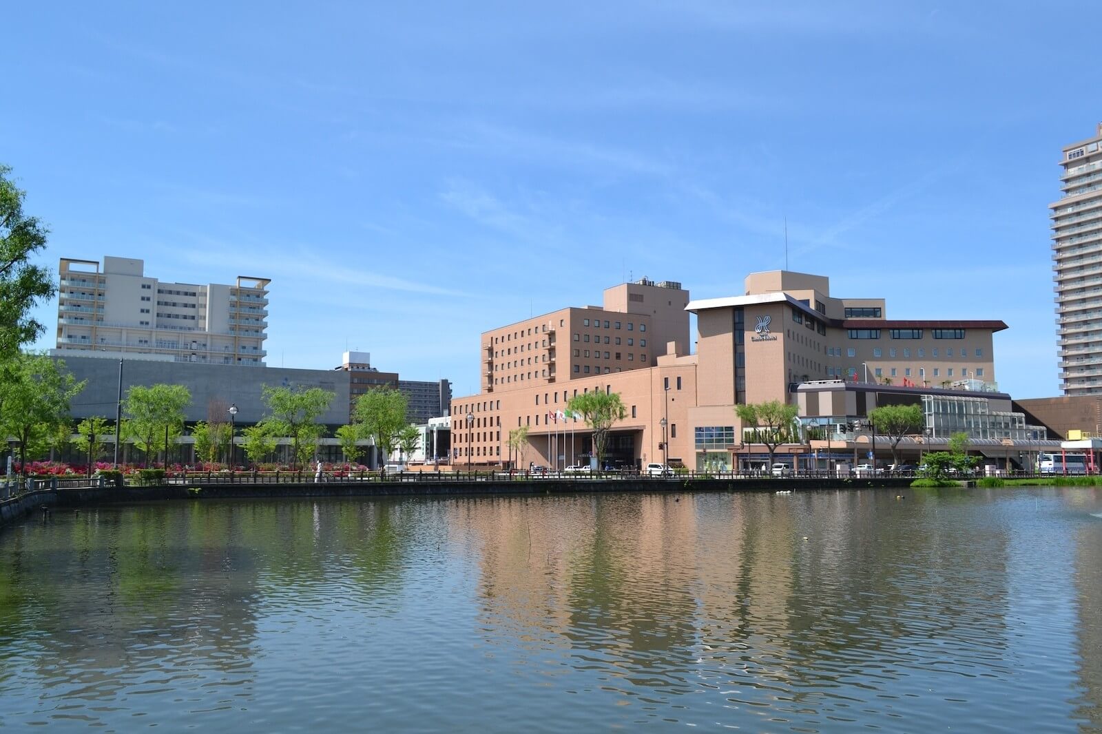 千秋公園のお堀越しに望むホテルの外観。中央にホテルの建物が立ち、水面に姿が映り込んでいる。左側には秋田県立美術館が見える。