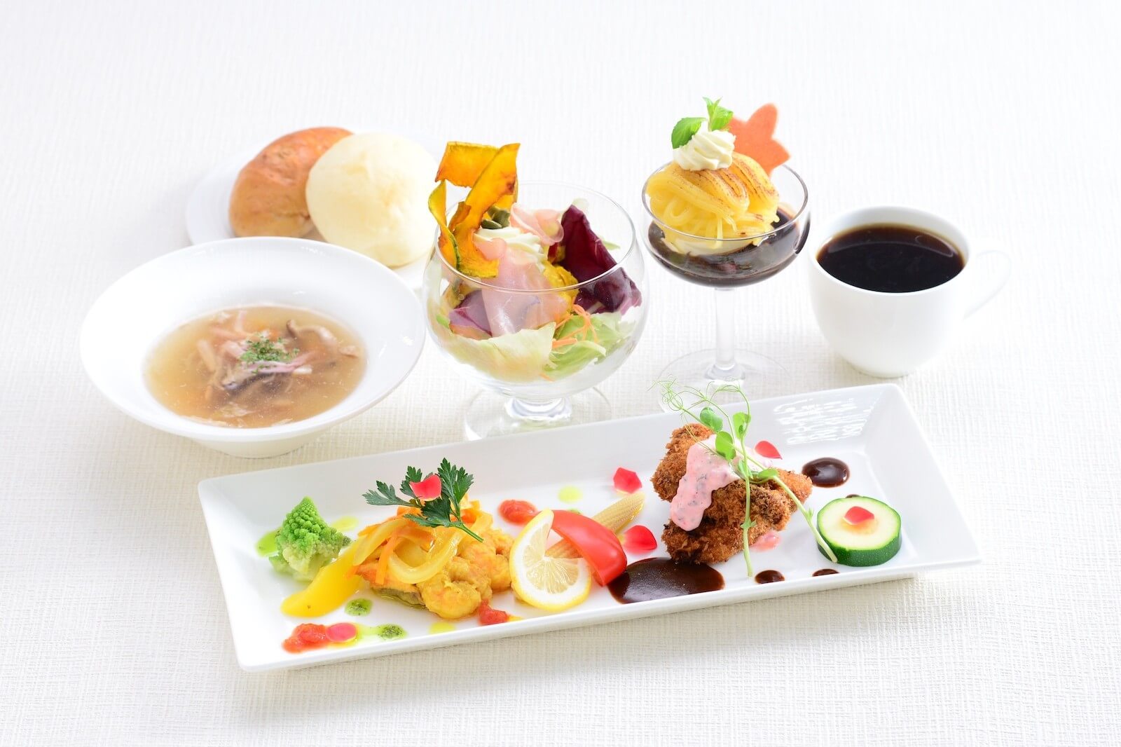 白いテーブルに並べられたランチコースの一例。前菜とメイン料理を盛り付けたプレートに、スープ、サラダ、パン、デザート、コーヒーが添えられている。秋田県立美術館とのコラボ企画「巨匠たちのパレット展」で提供されたランチ。