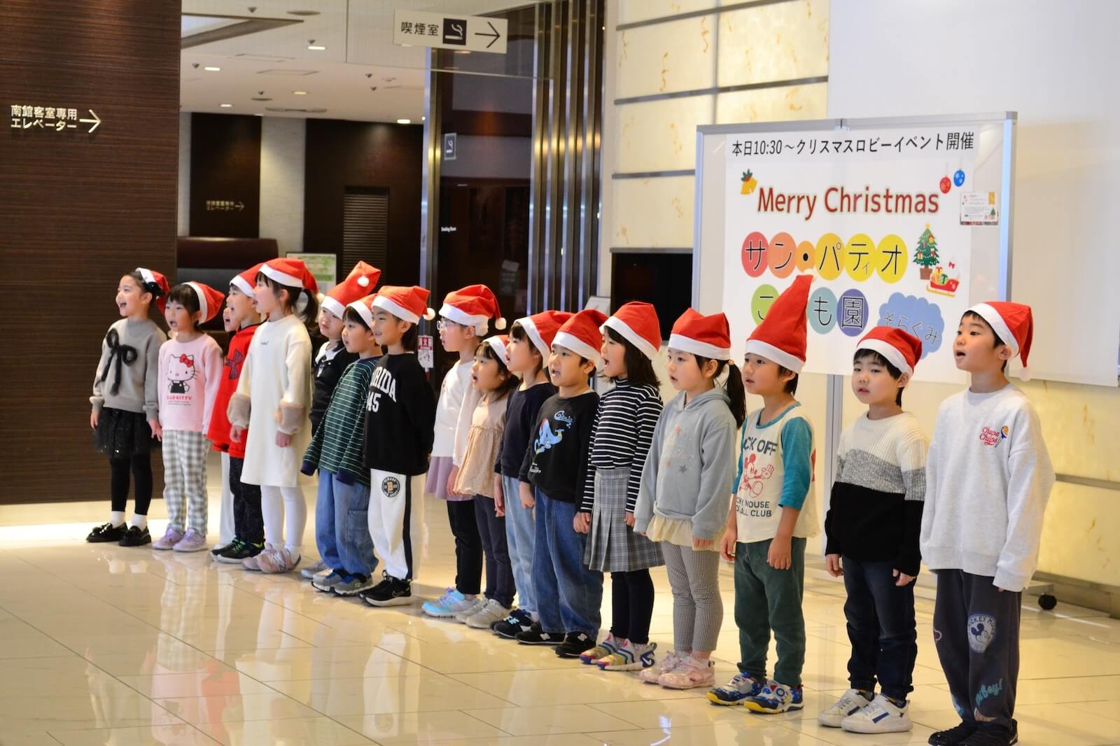 サンタ帽をかぶった子どもたちがロビーで並び、クリスマスイベントに参加している様子。秋田杉廃材を生かした装飾から展開した地域参加型の取り組みの一場面。