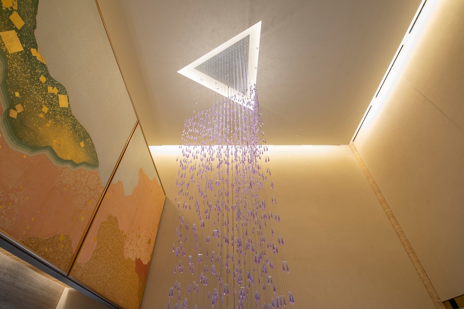 天井の開口部から垂れ下がる、藤の花をモチーフにした紫色のガラスパーツによるシャンデリア（リナ・ゴットメ氏の作品）