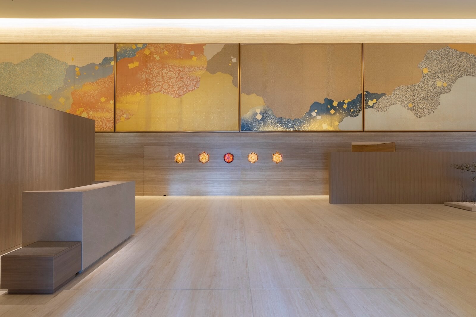 平安時代の和歌帖「三十六人歌集」の料紙をモチーフに、金箔調の文様や色面で構成された横長の壁面装飾が施されたロビー空間