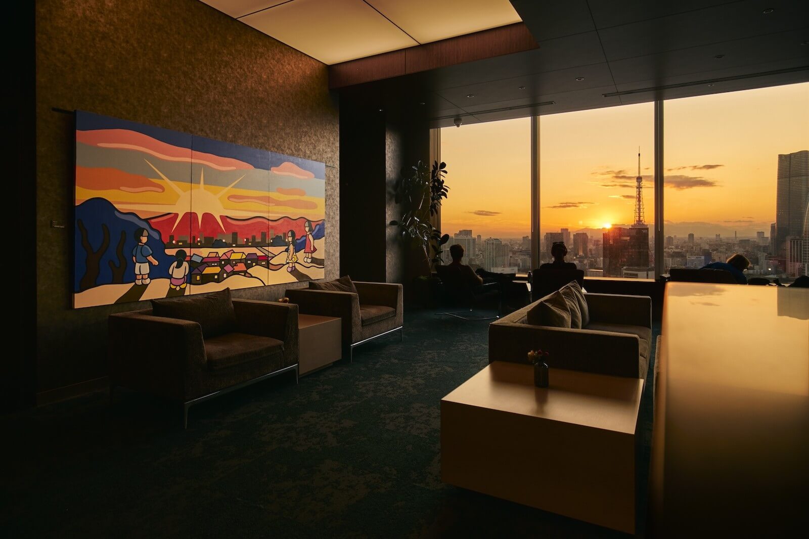 25階アトリウムのラウンジ空間。壁面にはカラフルな絵画が展示され、大きな窓の向こうに夕暮れの東京の景色が広がり、アートと眺望が一体となったギャラリー空間を形成している。