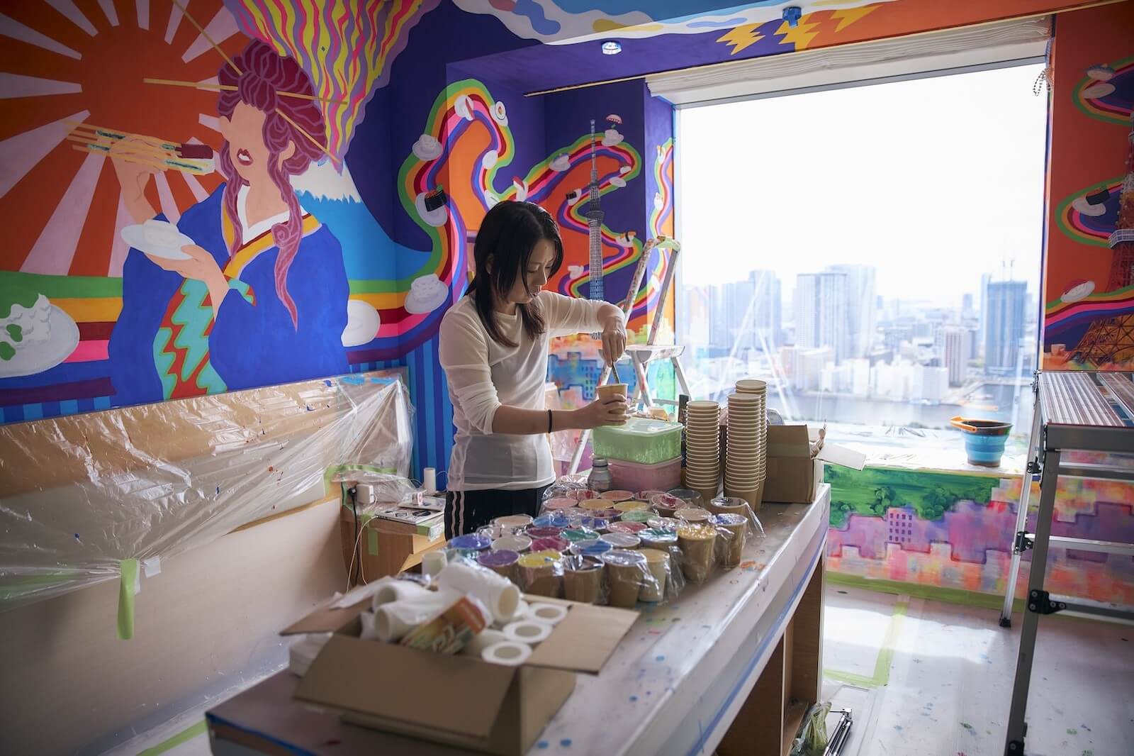 壁一面に描かれたカラフルな壁画の中で制作作業を行うアーティスト。