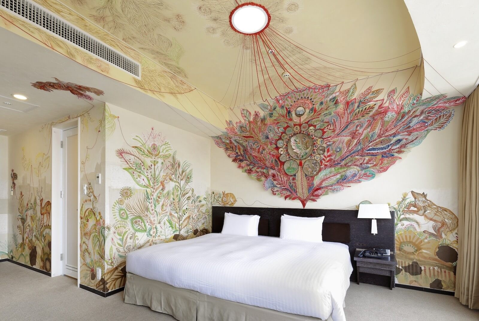 壁一面に繊細な植物モチーフの壁画が描かれたアーティストルームのベッドルーム。天井から広がる立体的な装飾が印象的