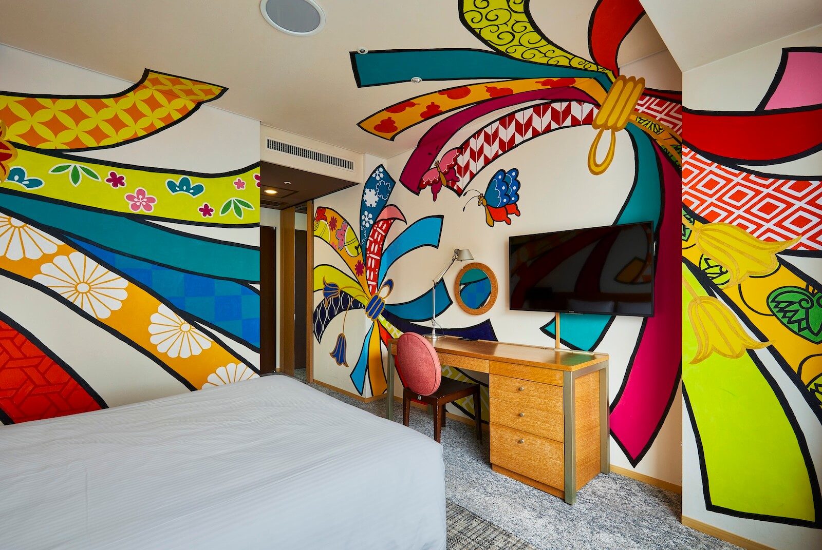 鮮やかな色彩と大胆な構図で描かれたパラリンアーティストによる壁面アートが施されたアーティストルームの客室