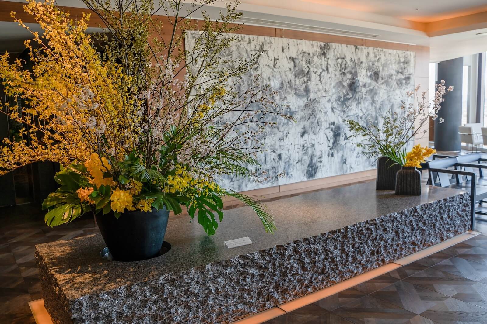 ロビー空間に展示された松井守男画伯の大型絵画作品。石造りの台座と生け花の前に据えられ、抽象的な画面が空間全体に強い存在感を放っている