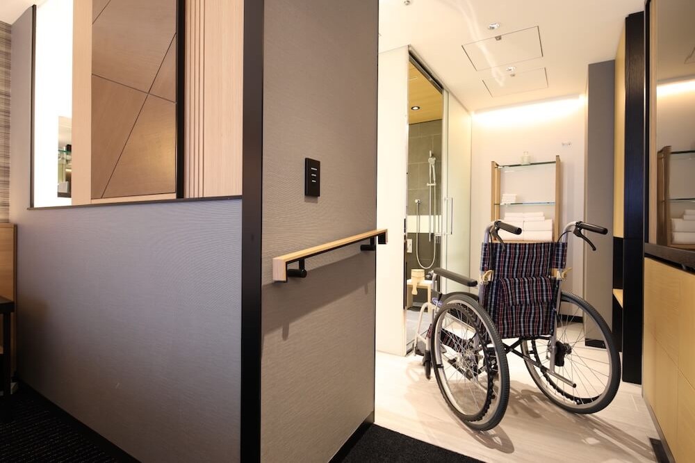 手すり付きの通路の先に、車椅子が入れる広さの洗面・シャワールームが見える。床は段差がない。