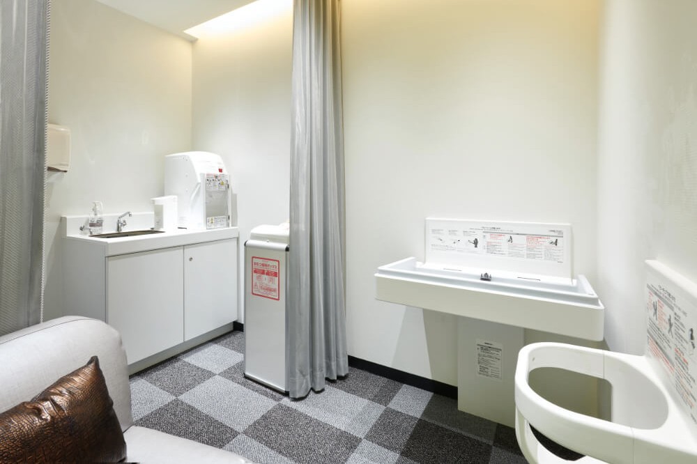 白を基調にした清潔な個室。手洗い台、給湯器、紙おむつ用ごみ箱、ベビーベッドとトイレが並んでいる。