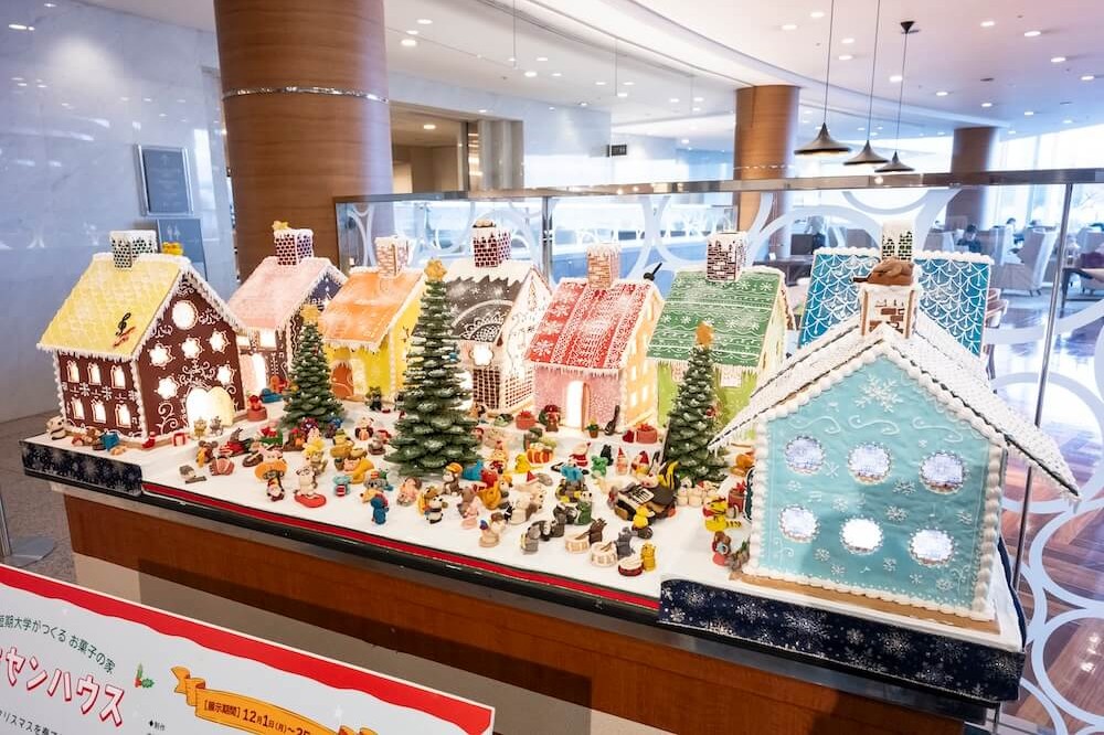 滋賀短期大学のパン・スイーツ研究サークルの学生が制作したヘキセンハウスの展示。色とりどりの菓子の家やツリー、ミニチュアで構成された街並みをホテルロビーに展示し、学生の創作活動と発表の場を提供している様子。