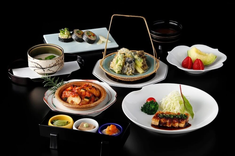和食のコース料理が並ぶテーブル。焼き物、煮物、天ぷら、寿司、茶わん蒸し、汁物、デザートまで多彩な料理が盛り付けられている。