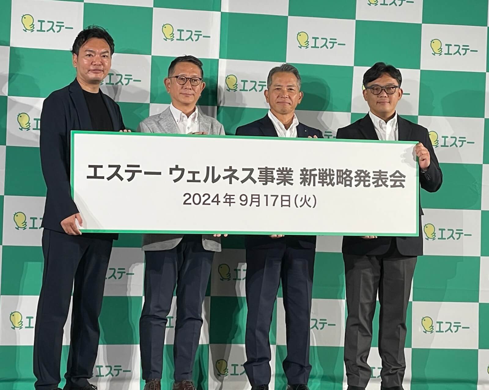 会場で登壇者が「エステー ウェルネス事業 新戦略発表会」2024年9月17日」と書かれたパネルを掲げている様子。