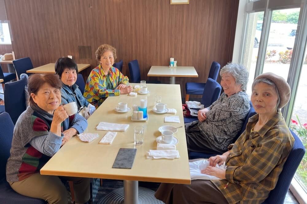 カフェのテーブルを囲み、コーヒーを飲みながら談笑する高齢女性グループの様子。