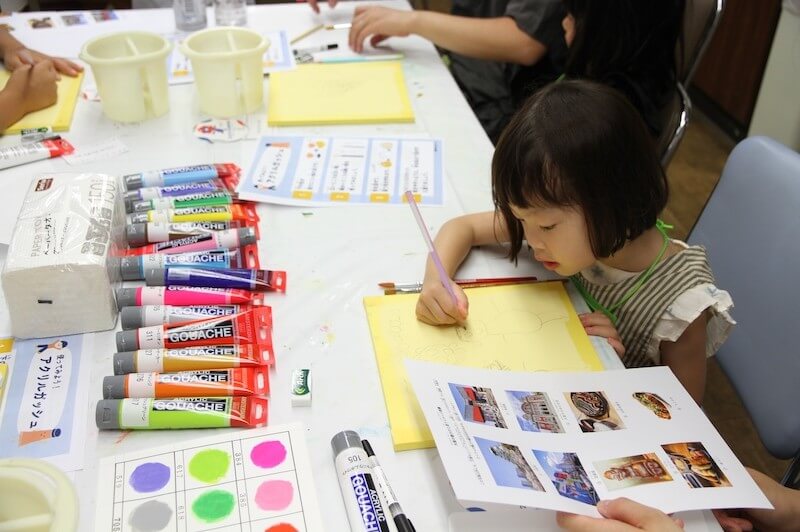 子どもが画材を使って紙に絵を描くワークショップの様子。