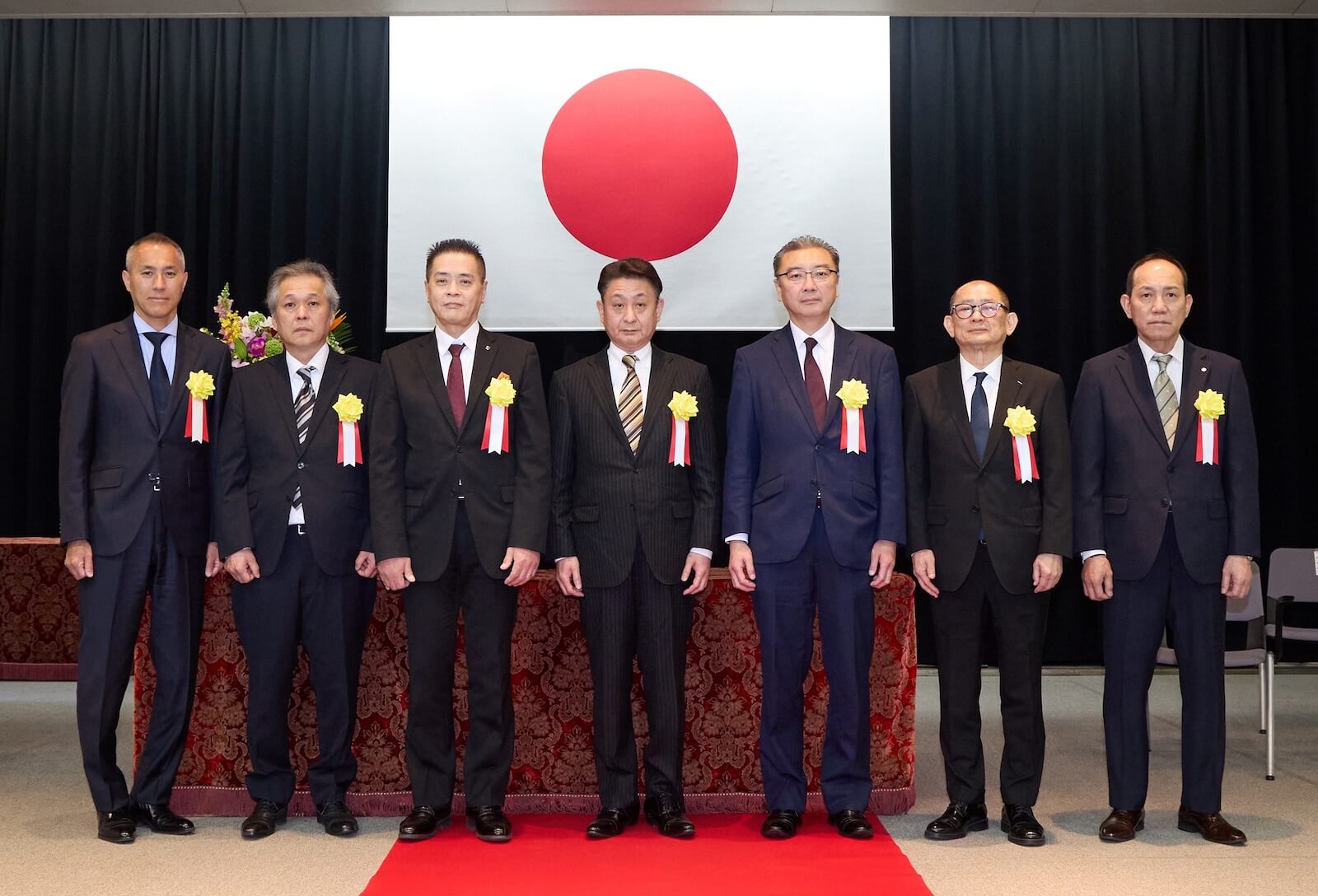 観光関係功労者国土交通大臣表彰式に出席した受章者ら7名の記念撮影。日の丸を背景に並んでいる様子。