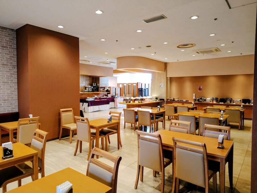 レストラン店内。木製のテーブルと椅子が並び、奥に料理を提供するビュッフェ台が設けられている。